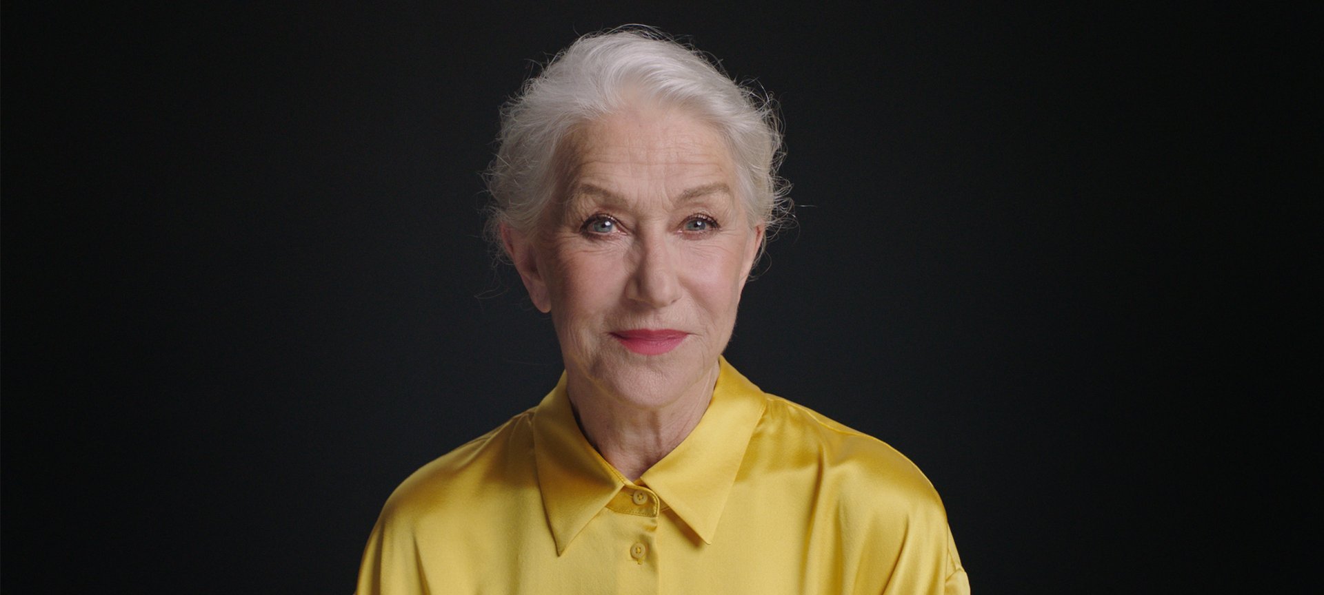 Portrait photo of Helen Mirren in front of black background.