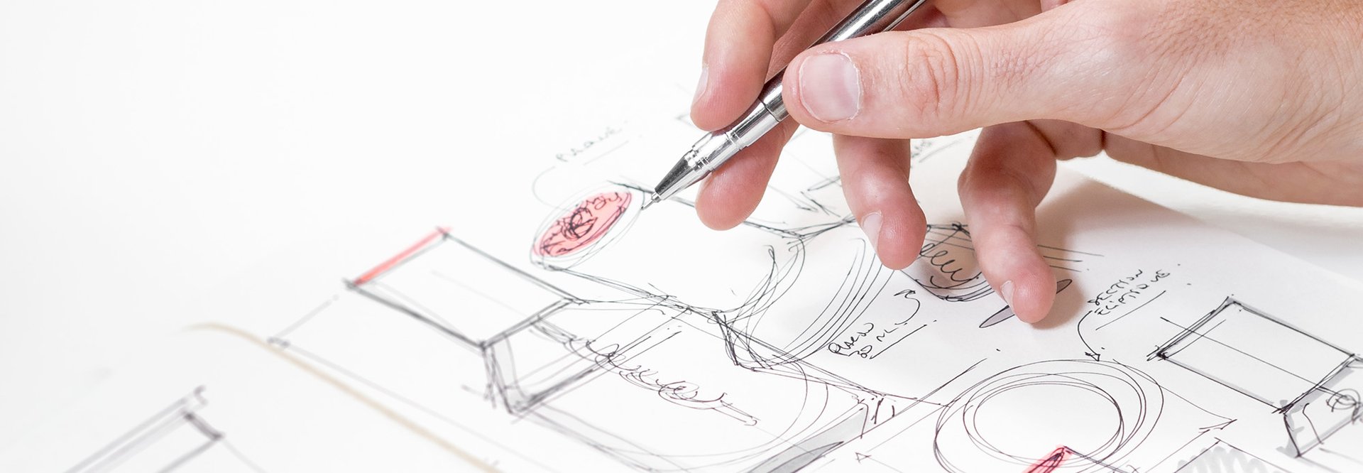 Close up of a hand holding silver pen over sketch of product packaging.